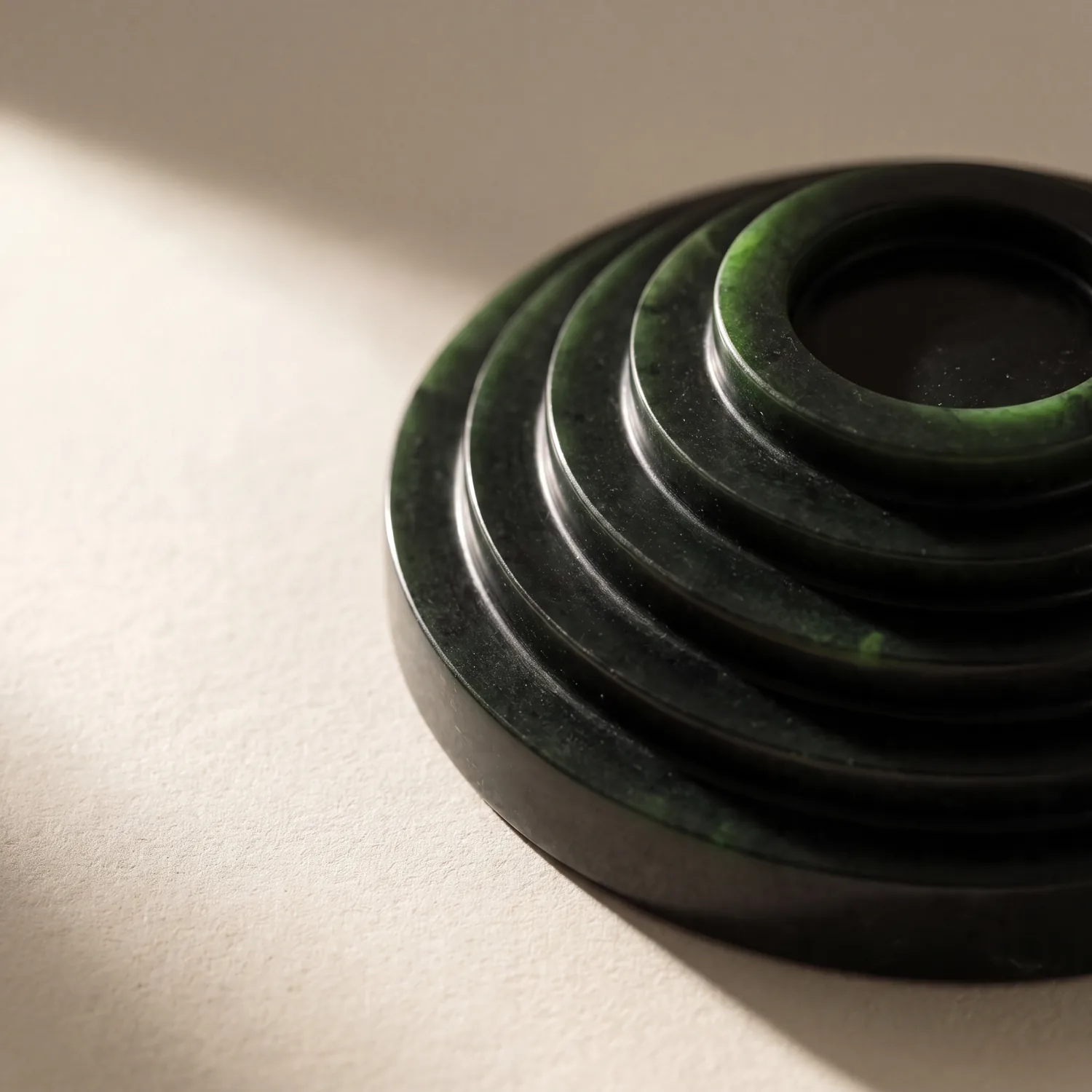 A polished dark green stone carved into concentric stepped terraces, raking light across the steps.